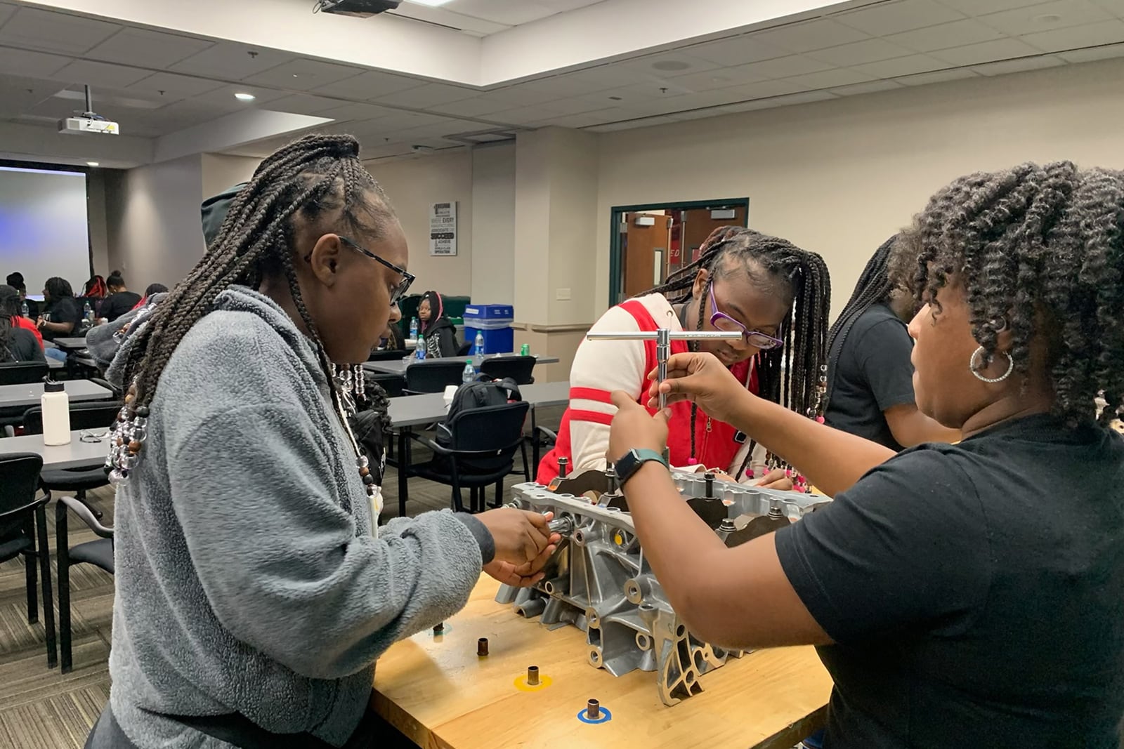 Two students and a school teacher in a classroom learning on a motor part.