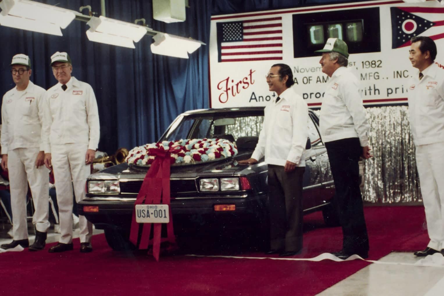 Honda employees posing for a photo with a beautiful classic Honda car model, with a sign dated November 1982 in the background.